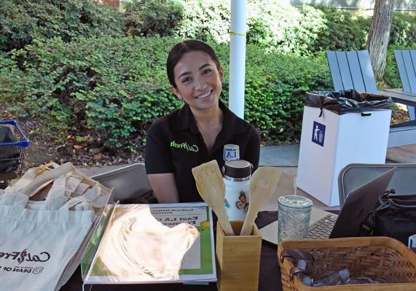 A person wearing a CalFresh polo sitting a table offering swag items.