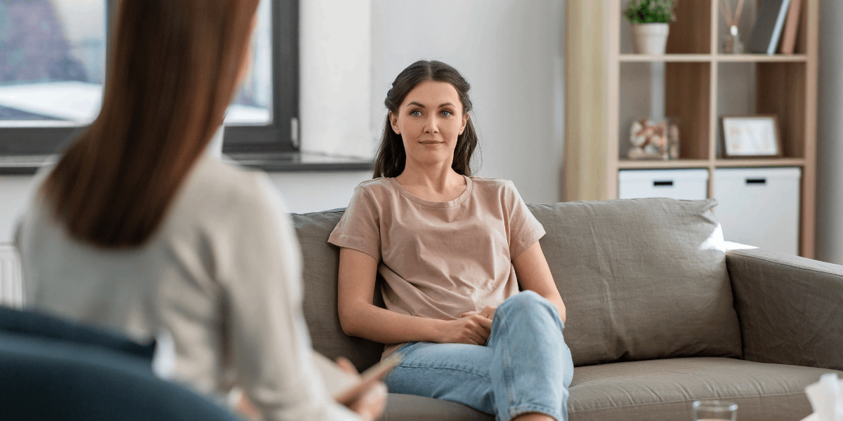 Women sits on sofa. Another woman sits across from her.