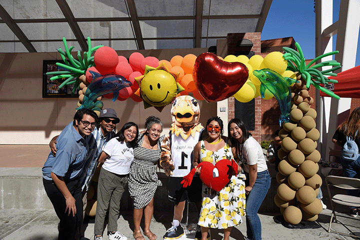 Group of people leaning in, posing in front of a large tropical balloon display.